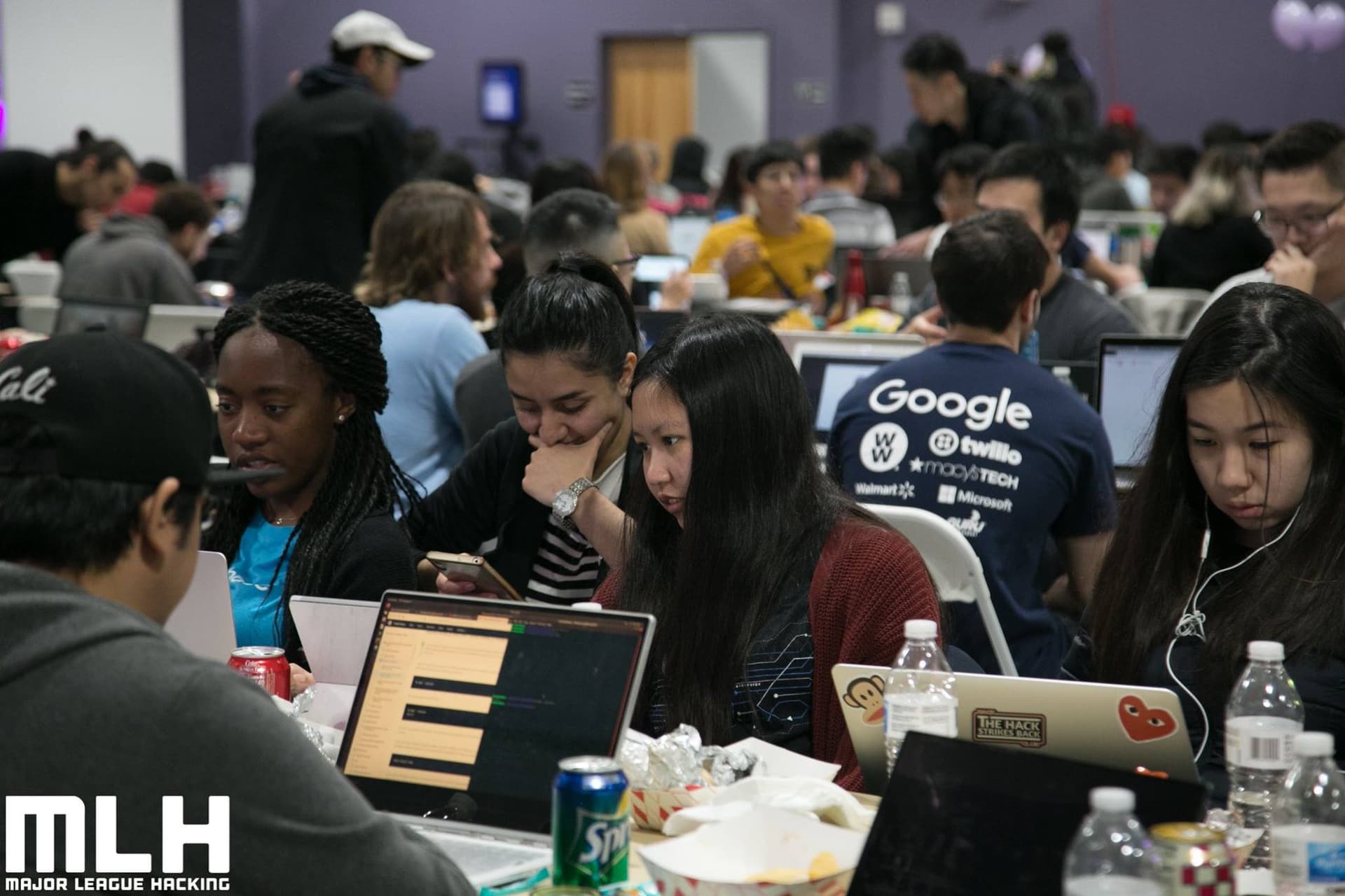 Crowded hackathon hall with participants working together on laptops at long tables