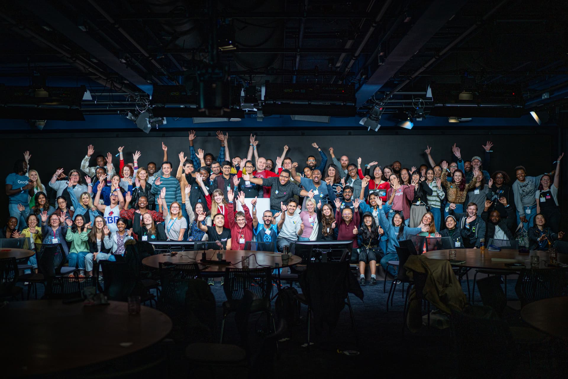 Large group photo of conference attendees on tiered seating with their hands raised